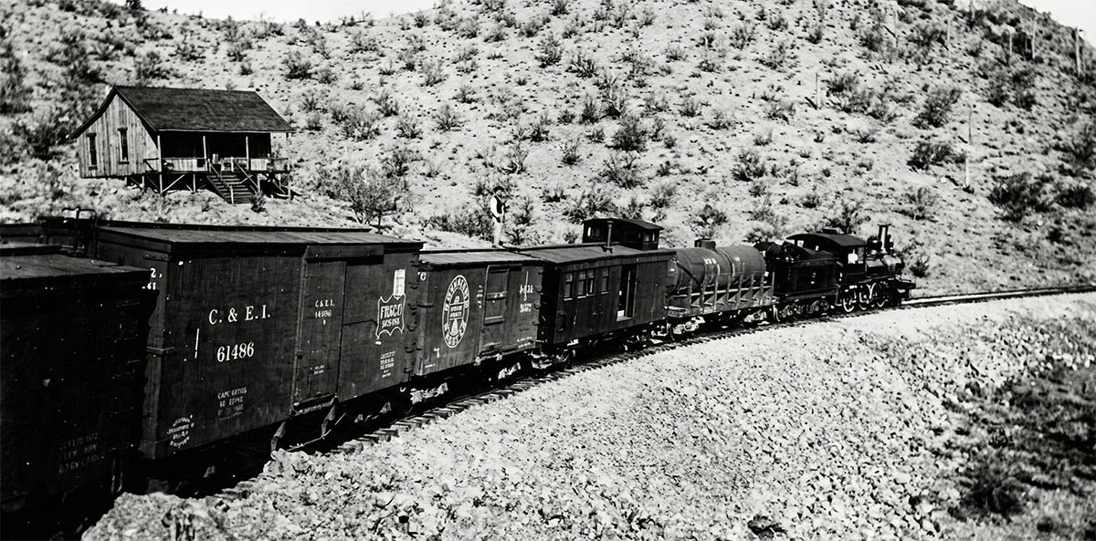 Digitally enhanced public domain black-and-white image of an early freight train hauling railcars through rugged Arizona terrain during the early 1920s